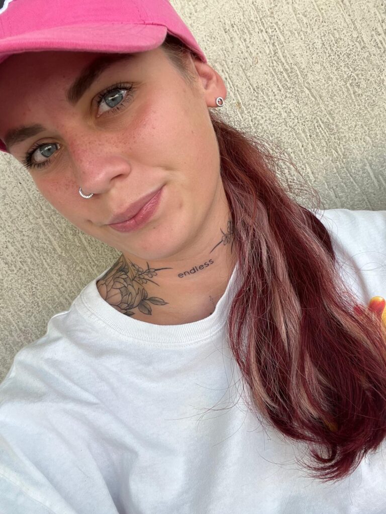 Natürliches Porträt einer Frau mit pinker Cap und roten Haaren, Nahaufnahme vor neutralem Hintergrund – authentische Portraitfotografie, minimi fotografie.